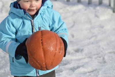 High angle view of boy holding basketball while standing on snow covered field