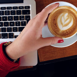 Cropped hand of woman holding coffee cup with laptop at table