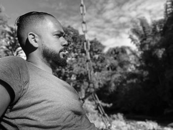 Side view of young man looking away against trees