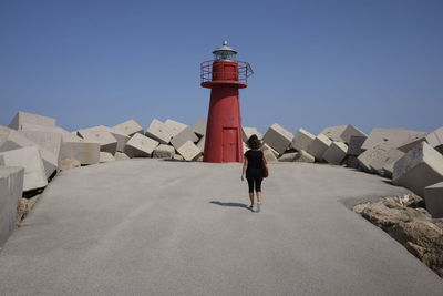 Rear view of woman walking by lighthouse against clear sky