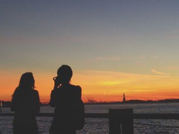 Silhouette couple standing by sea against clear sky during sunset