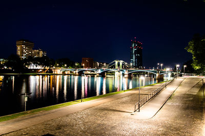 Illuminated bridge over river by buildings against sky at night