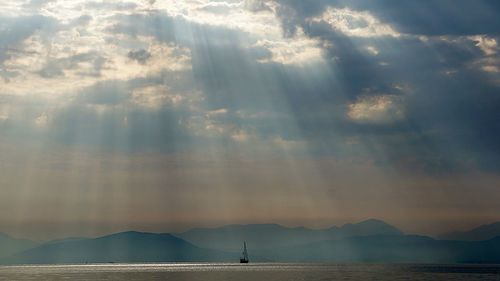 Distant boat sailing on sea against cloudy sky