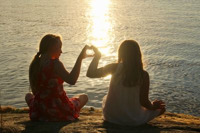 Rear view of women sitting on shore during sunset