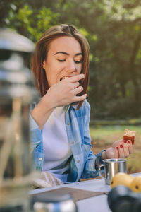 Woman holding eating food while sitting on chair at forest