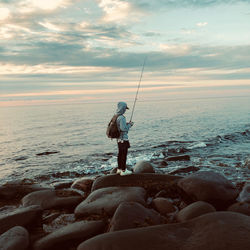 Man fishing on rock by sea against sky