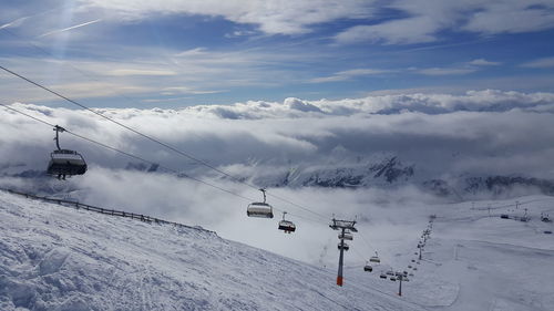 Ski lift over snow covered mountains against sky