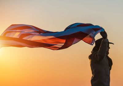 Low angle view of man waving flag against clear sky during sunset