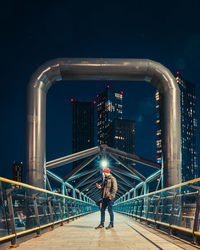 Rear view of man standing on illuminated bridge against sky at night