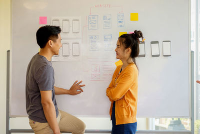 Side view of smiling business colleagues talking while standing by whiteboard