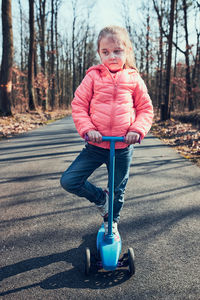 Full length of cute girl standing on scooter in forest