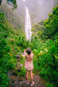 Rear view of woman standing by waterfall in forest