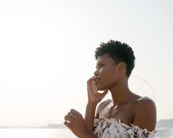 Woman using phone while standing by sea against clear sky