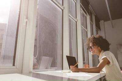 Side view of woman using laptop while standing in front of house