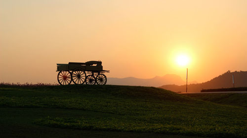 Silhouette built structure on field against orange sky