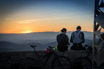 Rear view of men sitting on bicycle against sky during sunset