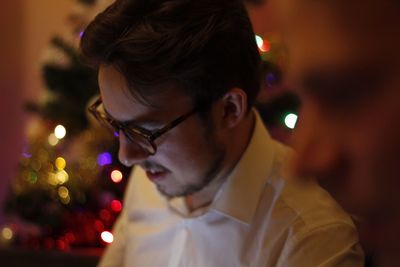 Smiling young man wearing eyeglasses sitting against christmas tree