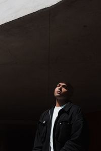 Young man looking away while standing against wall