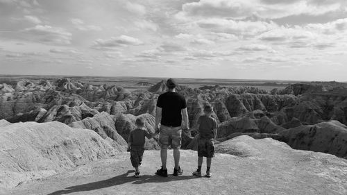 Rear view of father with sons on rock formation against sky