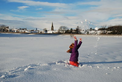 Teenage girl playing with snow against sky