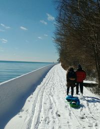 Rear view of people with sled on snow covered lakeshore