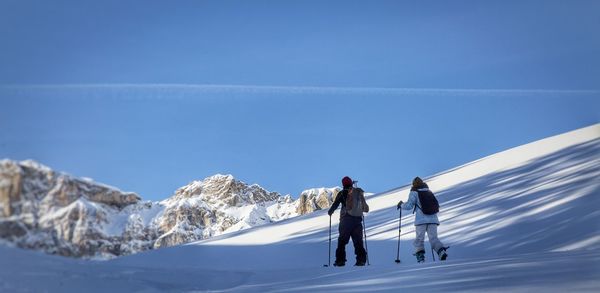 Rear view of people on snowcapped mountain against blue sky