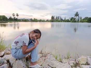 Man sitting by lake against sky