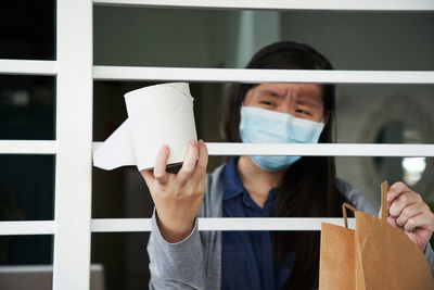 Portrait of young woman wearing face mask holding toilet roll