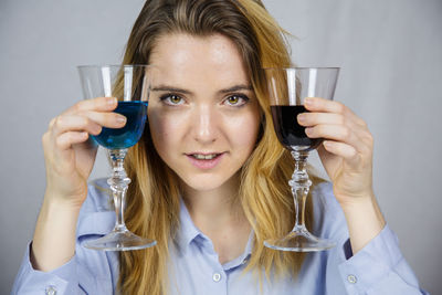 Portrait of young woman having drink in wineglasses against backdrop