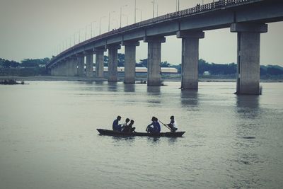 Men sitting on bridge over river against sky