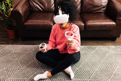 Full length of woman wearing virtual reality simulator sitting on floor at home