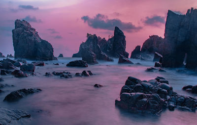 Rocks by sea against sky during sunset