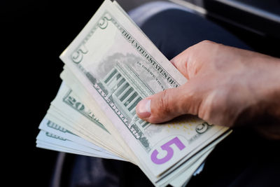 Cropped hand of man holding paper currency against black background