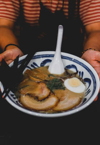 Close-up of hand holding tonkatsu ramen served in plate