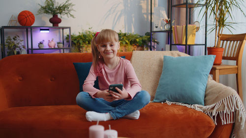 Young woman using digital tablet while sitting on sofa at home