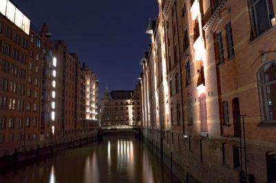 Illuminated buildings by canal at night