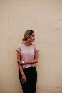 Woman looking away while standing against wall