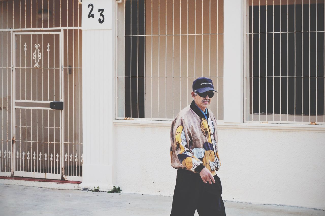 casual clothing, lifestyles, building exterior, architecture, built structure, young adult, full length, standing, young men, leisure activity, person, three quarter length, photography themes, holding, front view, technology, photographing, building
