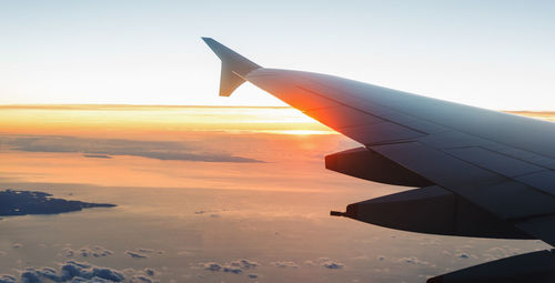 Airplane wing against sky during sunset