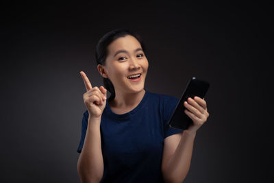 Portrait of young man using mobile phone against black background