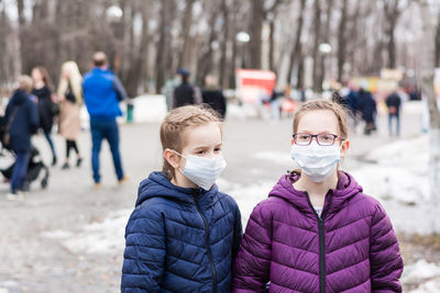 Two girls in protective face masks in the park, at a distance from the crowd of people