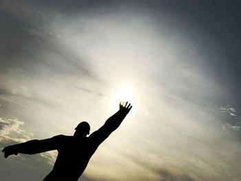 Low angle view of silhouette person with arms raised against sky