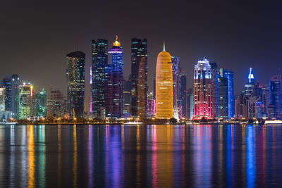 Illuminated city by river against sky at night