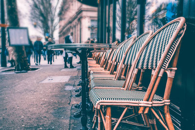 Empty chairs and tables at sidewalk cafe against buildings in city