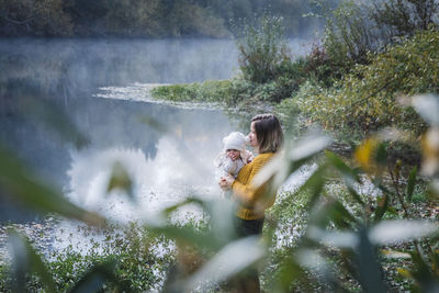 A woman is holding a baby near a river