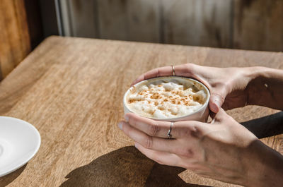 Cropped hands of woman holding coffee cup at table