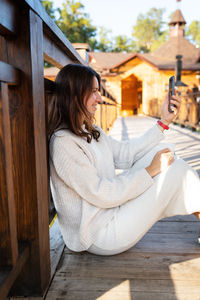 The girl is talking on the phone by videoconference while sitting on the street on a wooden bridge