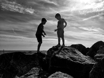 Full length of boys standing on rocks against sky