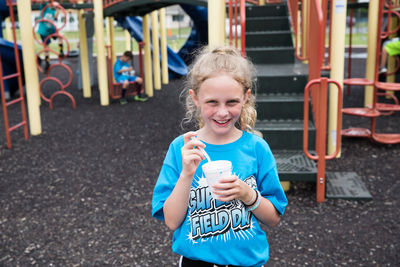 Smiling curly haired girl eats slush on school playground at field day