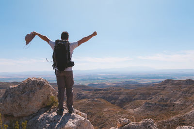 Rear view of man with arms outstretched while standing on rock against sky